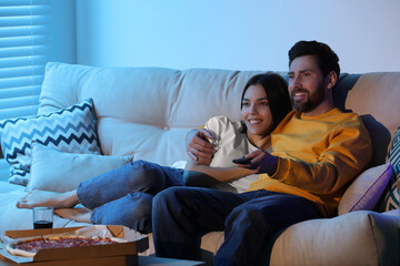 Happy couple watching TV with pizza on sofa indoors