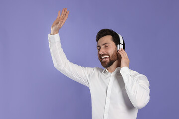 Fototapeta premium Happy man listening music with headphones on violet background. Space for text