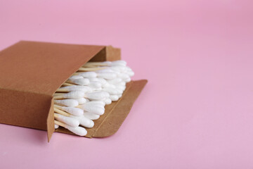 Box with wooden cotton buds on pink background. Space for text