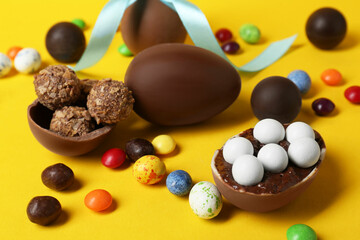 Tasty chocolate eggs and candies on yellow background