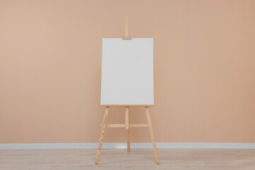 Wooden easel with blank canvas near beige wall indoors.