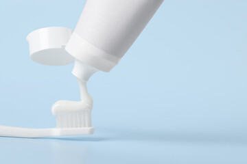 Applying paste on toothbrush against light blue background, space for text