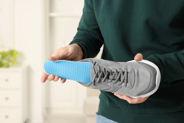 Obraz premium Man putting orthopedic insole into shoe indoors, closeup