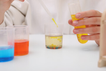 Girl mixing colorful liquids at white table indoors, closeup. Chemical experiment set for kids