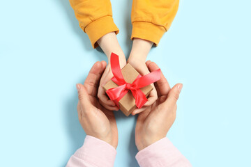 Mother giving gift box to her child on light blue background, top view