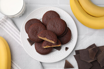 Tasty banana choco pies, pieces of chocolate, fruits and milk on white tiled table, flat lay