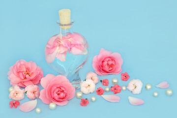 Rosewater for skincare with rose and carnation flowers, heart shaped bottle and pearls on blue. Balances natural skin oils, reduce redness, naturally hydrates skin treats rashes.