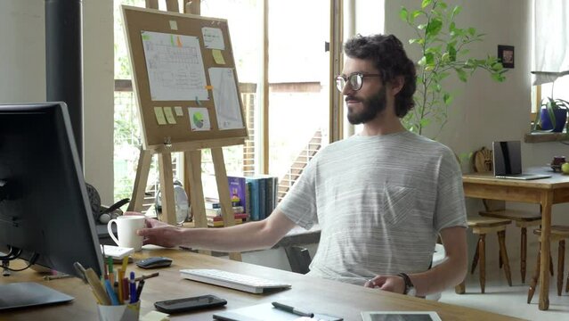 Designer is finishing his projects. He is done and ready to submit work he did. He push the button, grab cup of coffee and recline (lean back) to rest and enjoy moment after hard work.