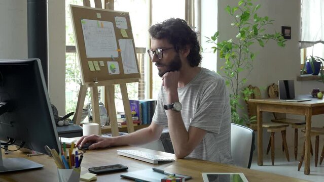 Man is working in studio. Sitting there all day is tiring. He looks in to the screen, takes off his glasses, rubs his red eyes. Job is very big monotony for him. He feels bad, unhappy and exhausted.