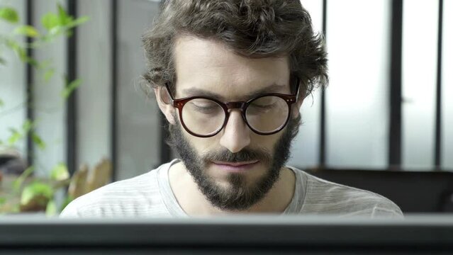 Young, attractive and beautiful aduld male person is writing with keyboard or reading information from the screen. His face relaxed and concentrated.