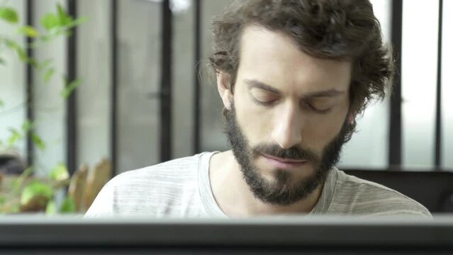 Young man intensively reading information on the screen. Adult could be designer, programmer, architect, student, who is working overtime hours at his studio, office or other kind of workplace.