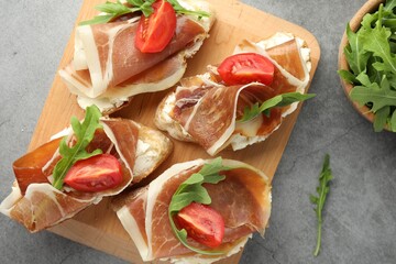 Tasty sandwiches with cured ham, tomatoes and arugula on grey table, flat lay