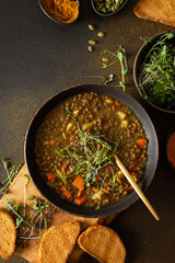 Healthy vegetarian lunches, brown lentil soup with tomatoes and carrots, potatoes and curry spices, toasted croutons, bowl with soup on cutting board on brown background