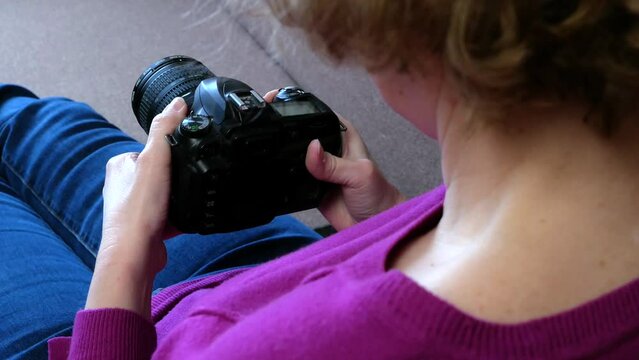 Beautiful photographer woman holding a digital camera sitting in the sofa at home, indoors