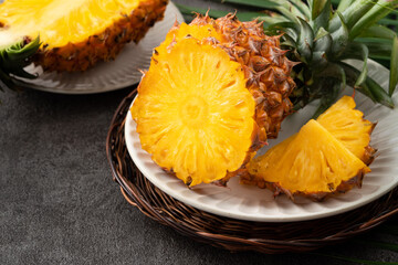 Fresh cut sliced pineapple in a plate over dark gray table background.