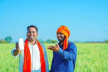 young indian farmer showing smartphone at agriculture field.