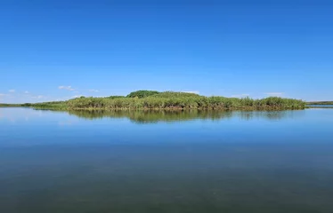 Foto op Canvas Outdoor summer nature landscape of a small island covered in green grass and reflected in the surface of a still lake under a clear blue sky. © Janice