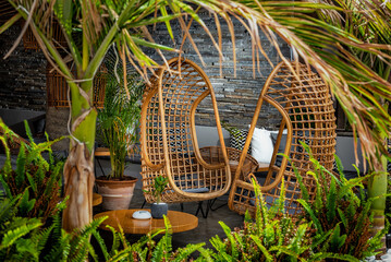 Hanging chairs in a restful oasis surrounded by lush greenery. Restaurant or hotel concept. 