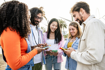 Multiethnic group of friends texting on their smartphones in the street. Diverse young people in a circle smiling and using their phones outside.