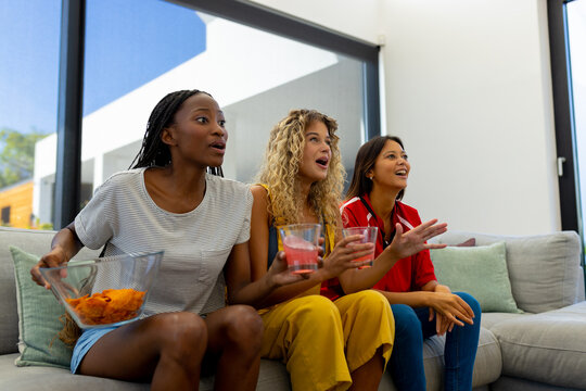 Group of excited diverse female friends sitting on sofa, watching sport on tv