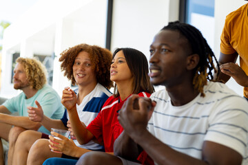 Obraz premium Group of happy diverse friends sitting on sofa, watching sport on tv