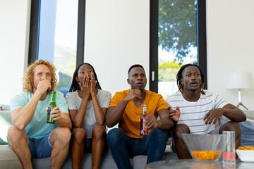 Group of excited diverse friends sitting on sofa, watching sport on tv
