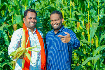 young indian farmer showing corn at corn field.