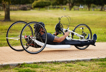 Health, cycling and fitness with man and handcycle on road for training, sports and challenge. Exercise, workout and marathon with person with a disability in park for cardio and wellness