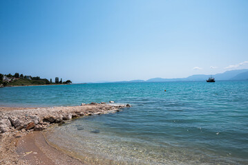 A rocky sand beach in Paleros, Greece with a boat peacefully floating on the turquoise sea. With its rugged beauty and crystal-clear waters, it offers a serene and captivating coastal experience