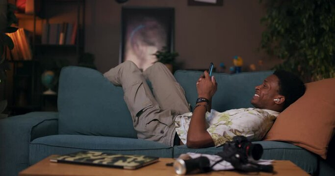 With cellphone in hand, the African man finds comfort on the couch in the living room, immersing himself in a playlist of energetic beats avid workout enthusiast, using music as a motivational tool.