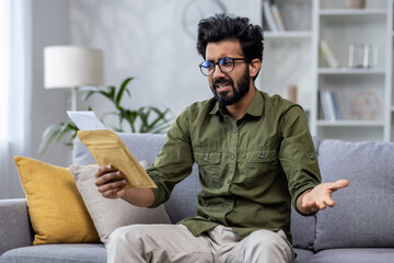 Upset and sad man at home received notification mail envelope with bad news, hindu man sitting on...