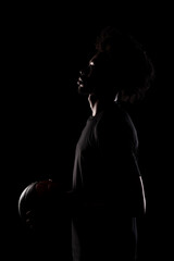 Fototapeta na wymiar Side lit silhouette of a basketball player. African American man holding basket ball posing against black background.