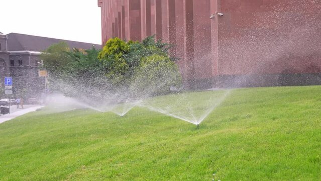 Garden Grass Watering. Smart garden activated with full automatic sprinkler irrigation system working in green park, watering lawn, flowers and trees sprinkler head rotation.