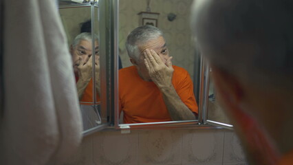 Senior man grooming himself in front of mirror during morning ritual. Domestic lifestyle of older...