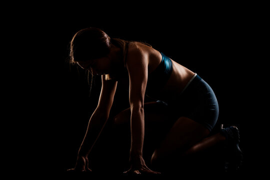 Female runner silhouette in low race start position. Girl in sportswear against dark background.