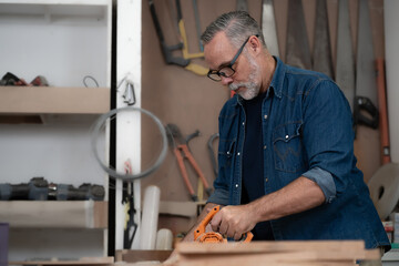 Bearded man carpenter working with skill in carpentry workshop. Professional joiner works with tools in woodworking. Portrait of mature woodworker making or repairing furniture. Craftmanship industry