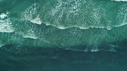 Aerial top shot of ocean waves break on a beach. Sea waves and beautiful sand beach aerial view drone shot.