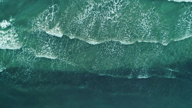 Aerial top shot of ocean waves break on a beach. Sea waves and beautiful sand beach aerial view drone shot.