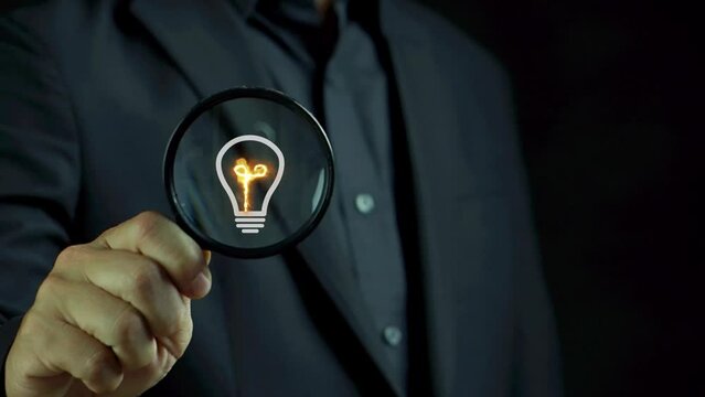 Businessman showing magnifying glass focus on glowing light bulb for creative thinking idea concept and future innovative technology. Knowledge, searching for new ideas, inspiration and imagination.