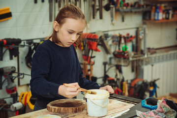 Cute boy makes wooden clock in the workshop. Young carpenter working with wood in craft workshop.