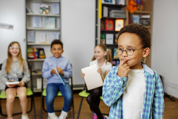 Schoolboy standing in middle of classroom and answering question in front of classmates and teacher.