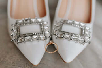 white women's shoes with Swarovski stones, a gold women's engagement ring with a diamond is next to it. Close-up