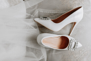 white women's shoes with Swarovski stones, standing chaotically, next to the bride's veil. Close-up photo