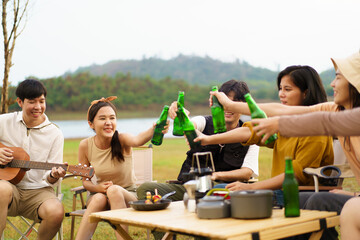 Group of Asian young adult people enjoy drinking a beer together during camping at the park. Asian young women and men celebrating with a bottle of a beer together.