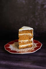 a piece of carrot cake, a layer with white cream on a ceramic plate on a dark background