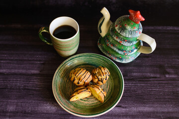 eclairs with a cut and cream, on a ceramic green plate next to a cup of coffee and a teapot