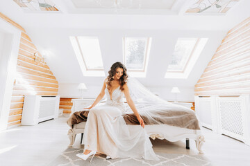 Beautiful bride in wedding dress sitting on bed in her bedroom. Nice waist. Classic interior