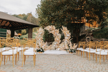 Wedding ceremonies in the park for the bride and groom. The arch is made of fresh flowers and dry reeds. Away wedding ceremonies. Chairs with gold color