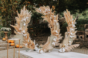 Wedding ceremonies in the park for the bride and groom. The arch is made of fresh flowers and dry reeds. Away wedding ceremonies. Chairs with gold color