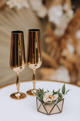 Gold wedding rings on a glass box decorated with rose flowers, next to it are wedding glasses in gold color